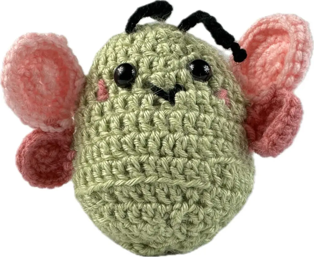 Photograph of a crocheted green butterfly with pink wings against a white background